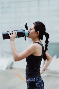 夏季户外锻炼时，一名亚洲女子正在休息补水