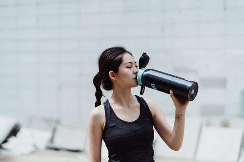 Free Young woman in workout attire drinks from a water bottle, promoting healthy lifestyle. Stock Photo