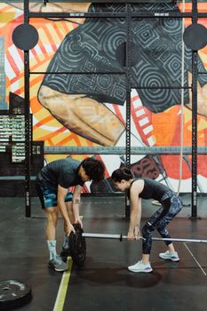 Two adults lifting weights together in a gym with vibrant wall art, showcasing teamwork and strength.