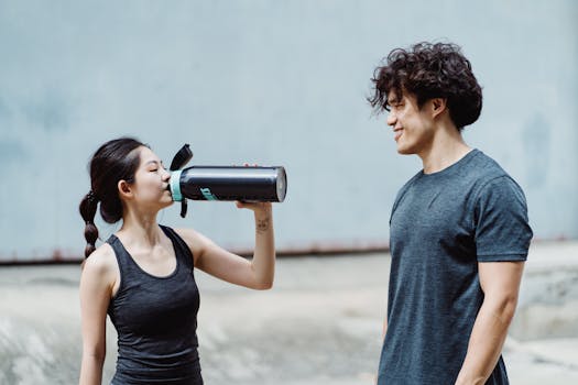 A young man and woman enjoy an outdoor workout session, sharing a moment of hydration and camaraderie.