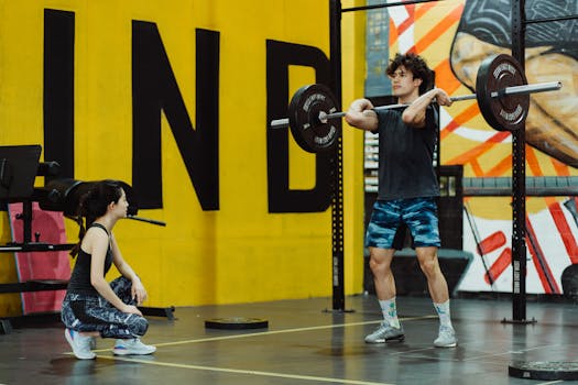 Two young adults engaging in weightlifting at a vibrant gym setting.