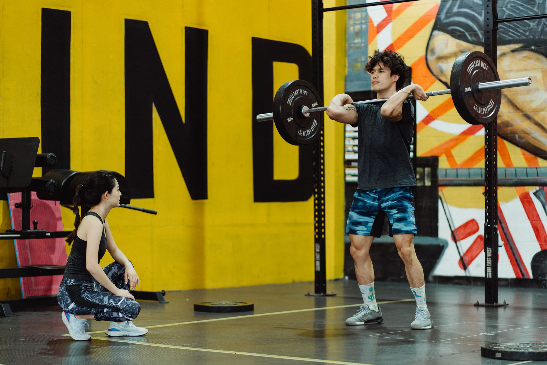 Two young adults engaging in weightlifting at a vibrant gym setting.