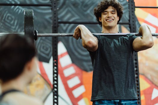 A young man confidently lifts a barbell in a vibrant gym setting, showcasing strength and joy.