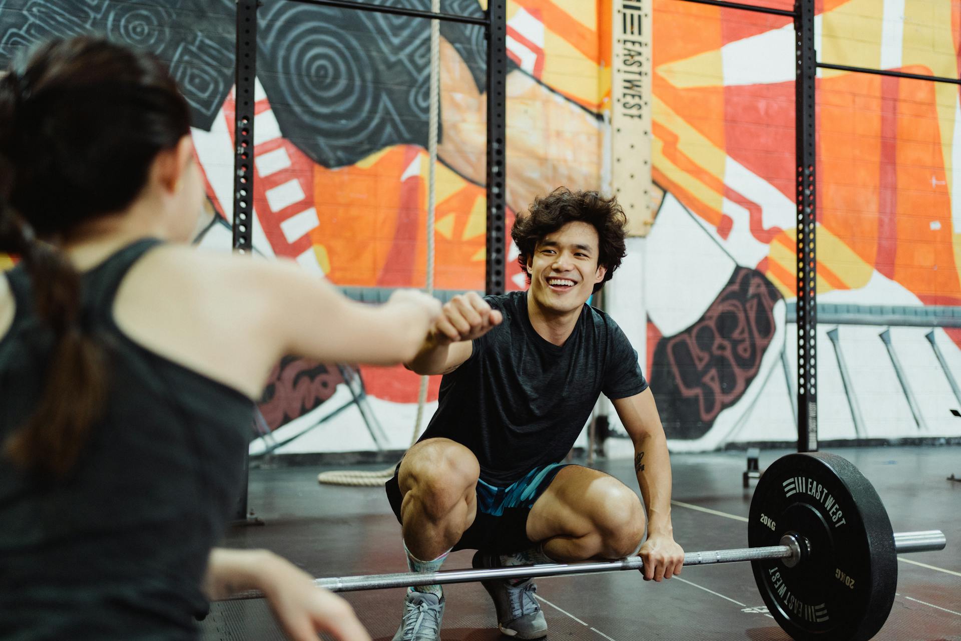 A man and woman share a motivational fist bump in a colorful gym setting.