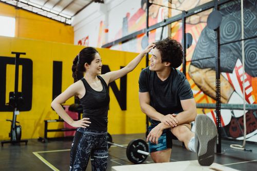 Free A couple engaged in a playful moment while stretching at a colorful gym. Stock Photo