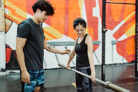A man coaches a woman in a gym on barbell lifting techniques, highlighting fitness and training.