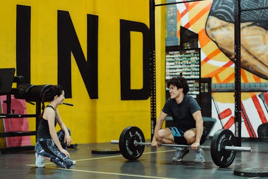 Two young adults in a gym participating in a weightlifting session, sharing a positive moment.