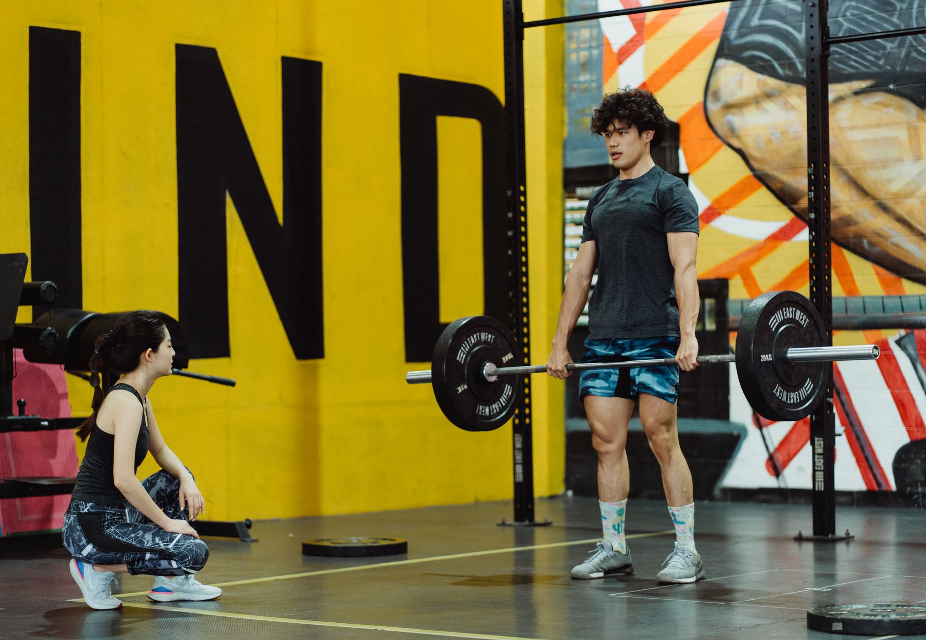 Man performing deadlift in the gym while female trainer watches, showcasing strength and fitness.