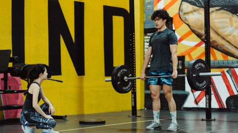 Man performing deadlift in the gym while female trainer watches, showcasing strength and fitness.