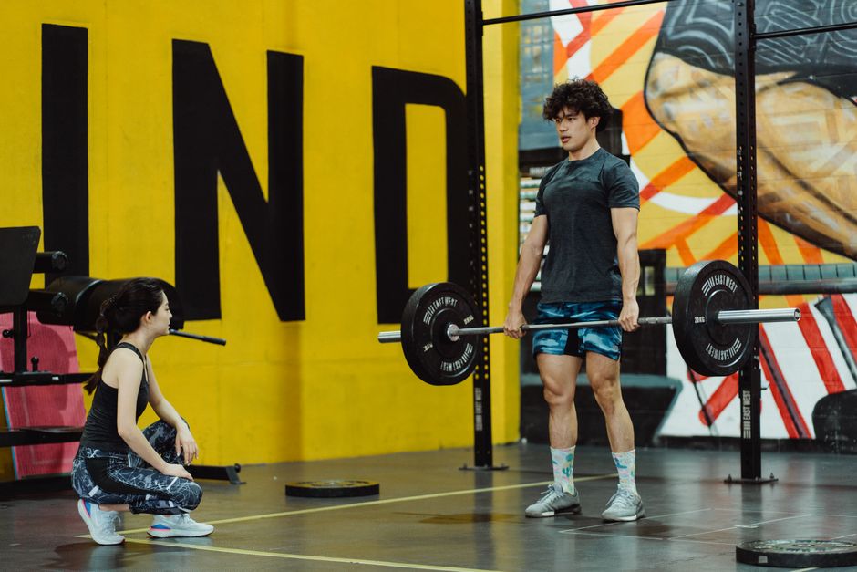 Man performing deadlift in the gym while female trainer watches, showcasing strength and fitness.