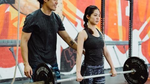Young Asian couple lifting barbells in a colorful indoor gym setting.