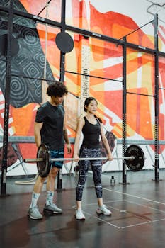 Two athletes lifting weights in a colorful, modern gym setting. Indoor workout session.