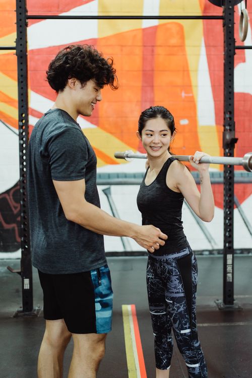 Free A man and woman performing barbell exercises together in a colorful gym. Stock Photo