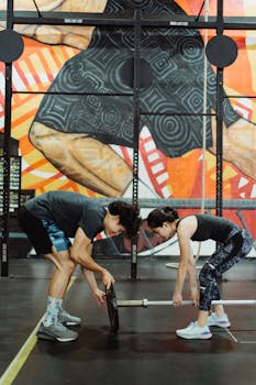 Two adults preparing weights in a colorful gym setting, showcasing teamwork.