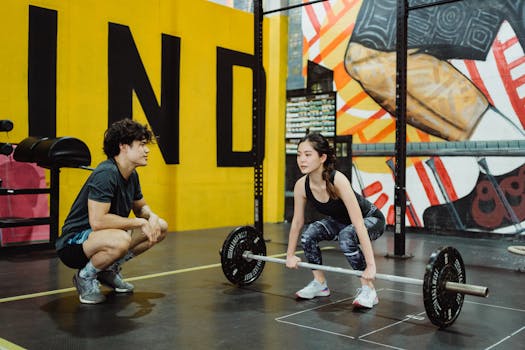 A young woman lifting weights guided by a trainer in a colorful gym setting.