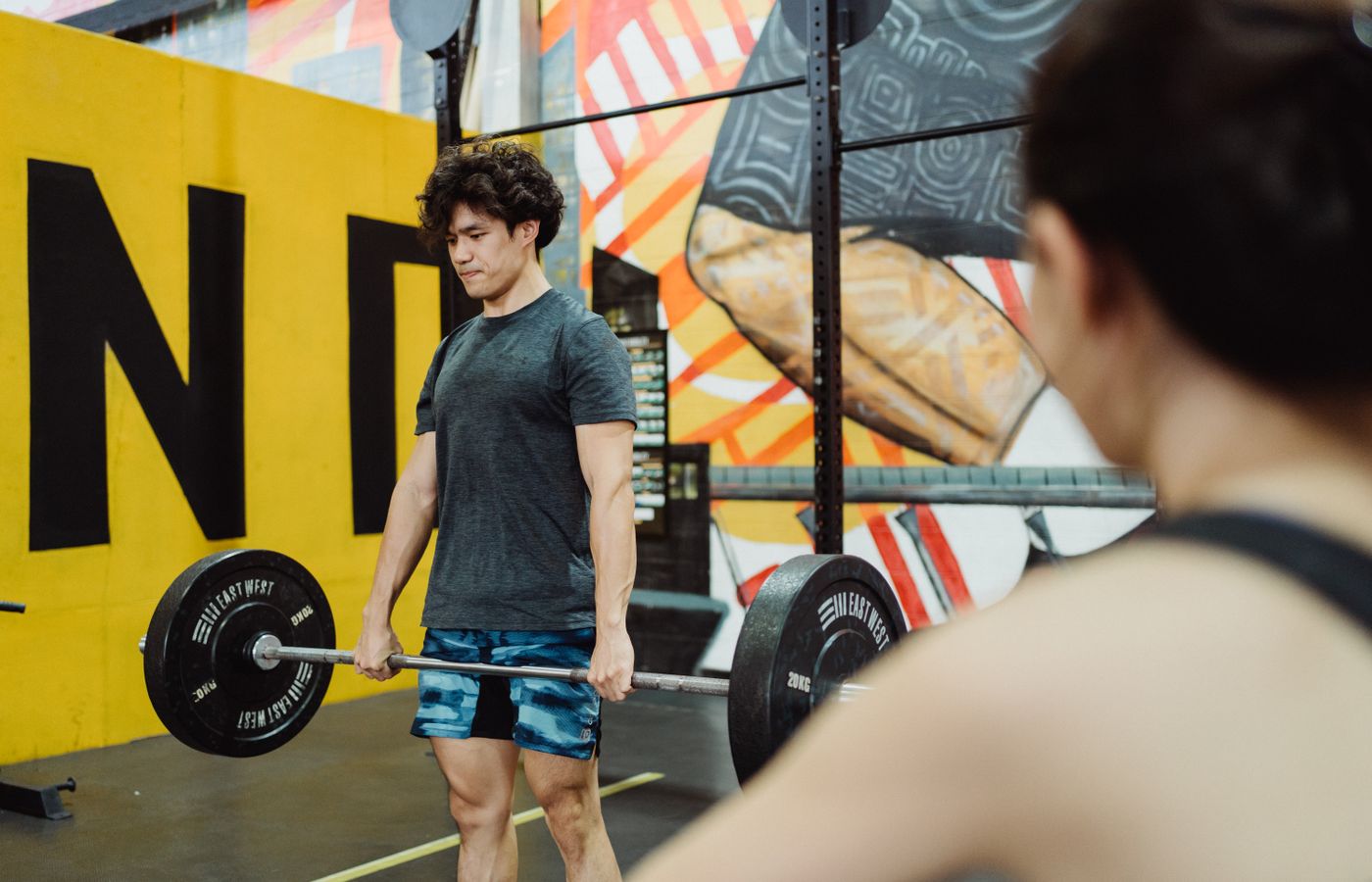 Muscular man lifting weights in an indoor gym with vibrant murals, embodying strength and focus.