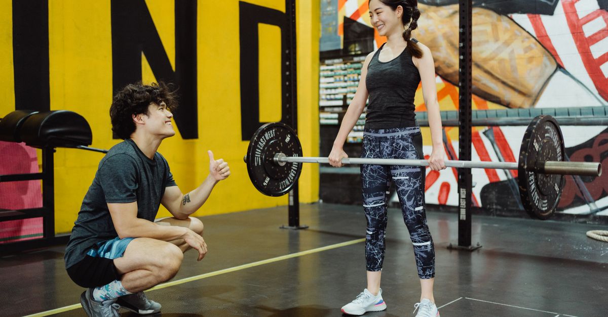 Young woman lifting weights with trainer guidance indoors, showcasing fitness and motivation.