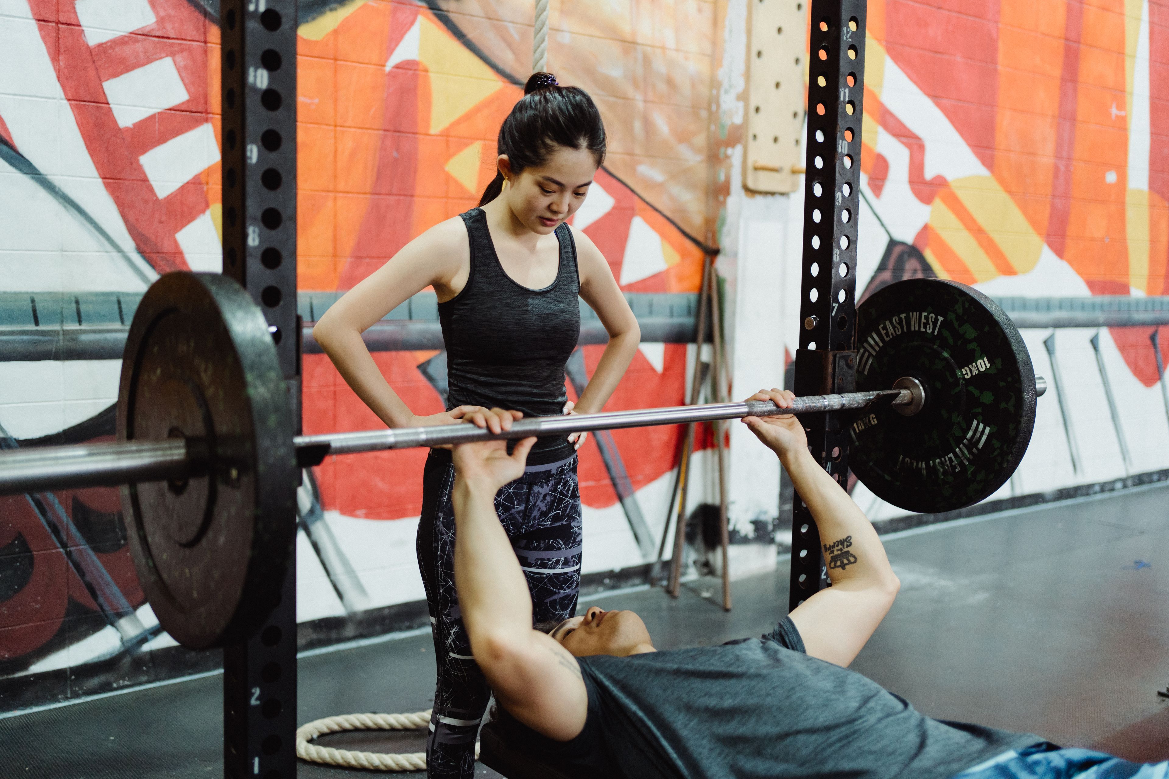 A man and woman working out together with bench press in a vibrant gym setting.