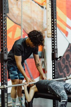 A personal trainer helps a client during a bench press session in a modern gym.