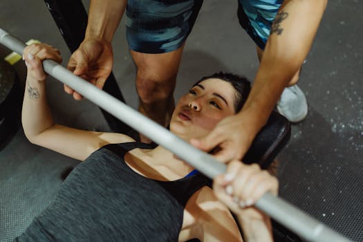 Woman performing bench press exercise with guidance in a gym setting.