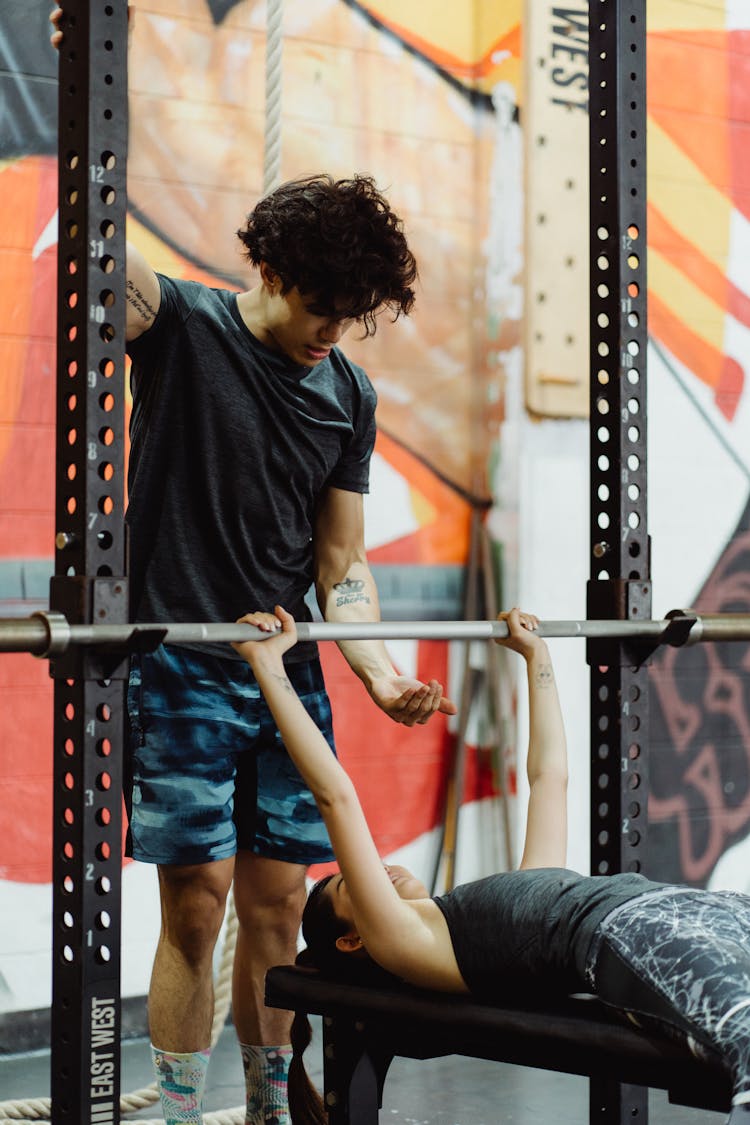 Photo Of A Man In A Gray Shirt Helping A Woman Doing Bench Press