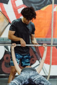 A personal trainer helps a woman with weight lifting at an indoor gym.