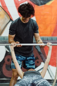 A coach helps a woman bench press in a vibrant gym setting, emphasizing fitness and teamwork.