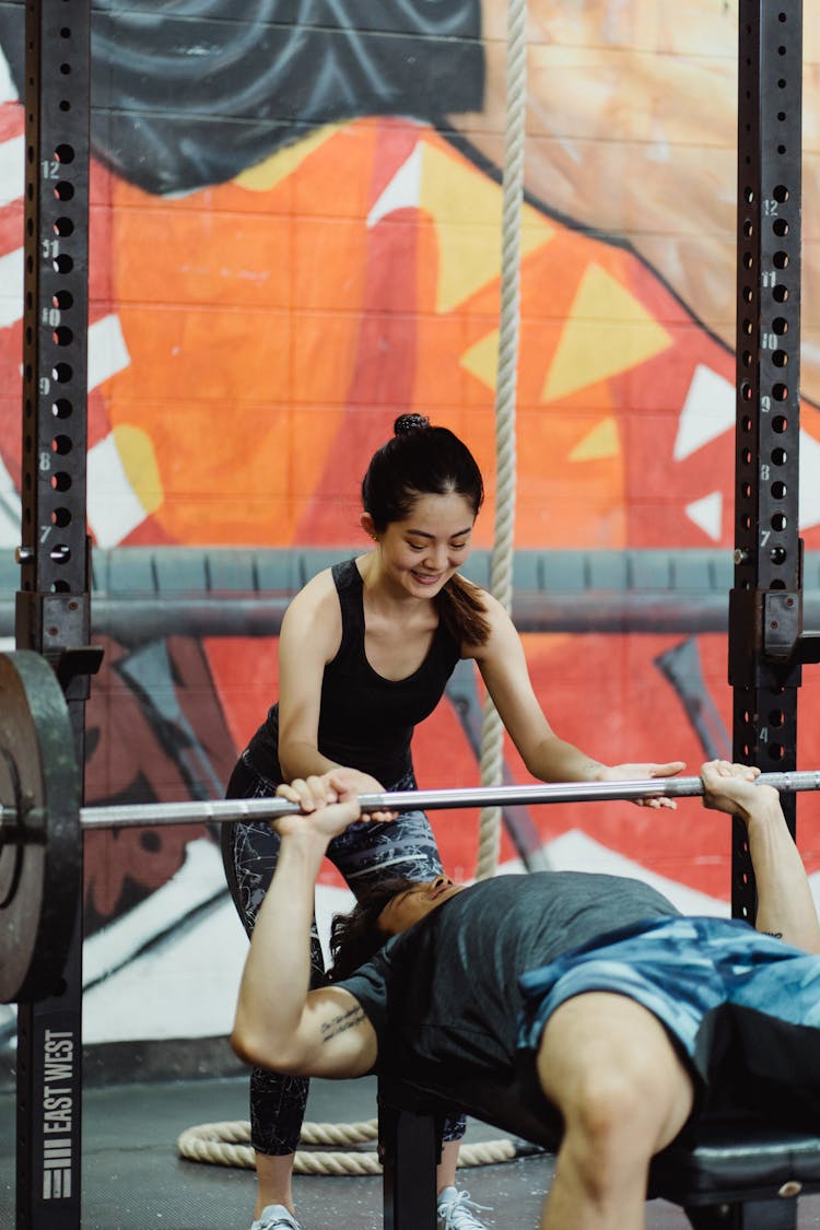 Photo Of A Woman In A Black Tank Top Helping A Man Doing Bench Press