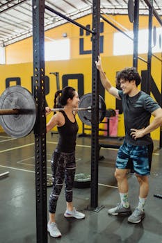 A couple in activewear exercising together at the gym with barbells.