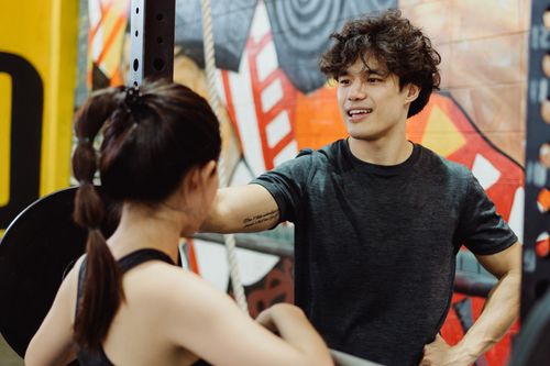 Free Two young adults in a gym engaging in a lively fitness discussion with a vibrant mural in the background. Stock Photo