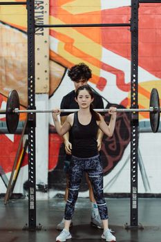 Female weightlifter with a trainer in a gym, focused on perfecting form.