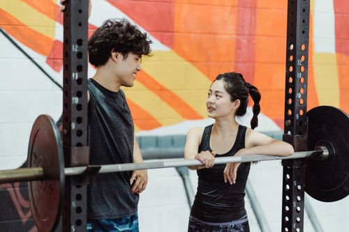 Free A young couple interacts at a gym while leaning on a barbell, promoting fitness and teamwork. Stock Photo