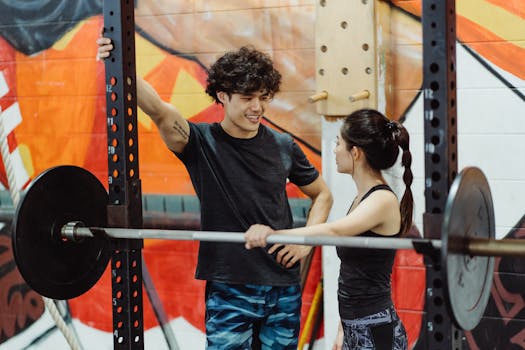 A fit couple in activewear chatting at the gym with a barbell setup.