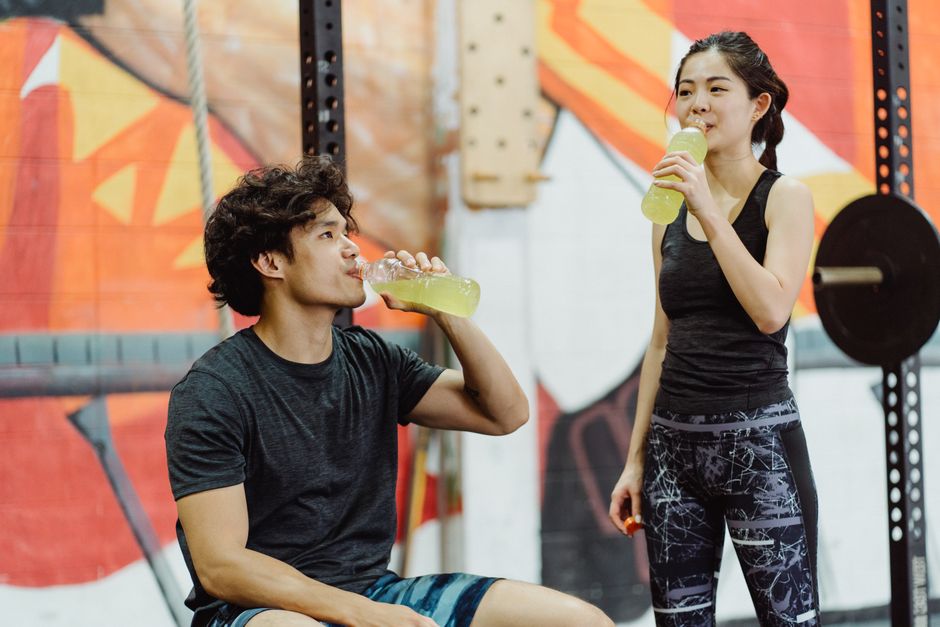 Two people in gym attire drinking recovery shakes after a workout.