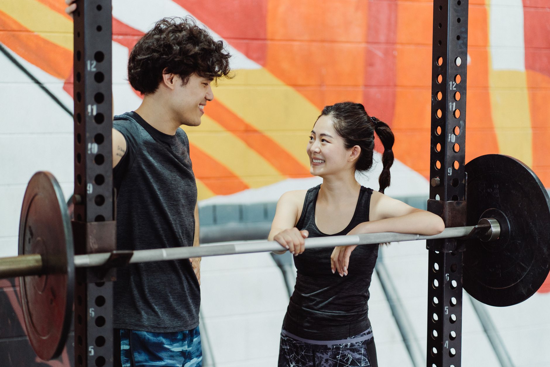 Couple enjoying a workout at the gym, sharing a moment while leaning on a barbell.
