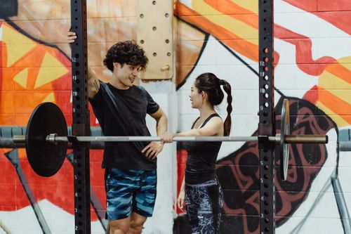 Free A man and woman talking near gym equipment with colorful graffiti background. Stock Photo