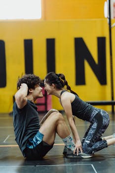 An Asian couple enjoys a fitness routine, enhancing closeness with sit-ups in a gym setting.