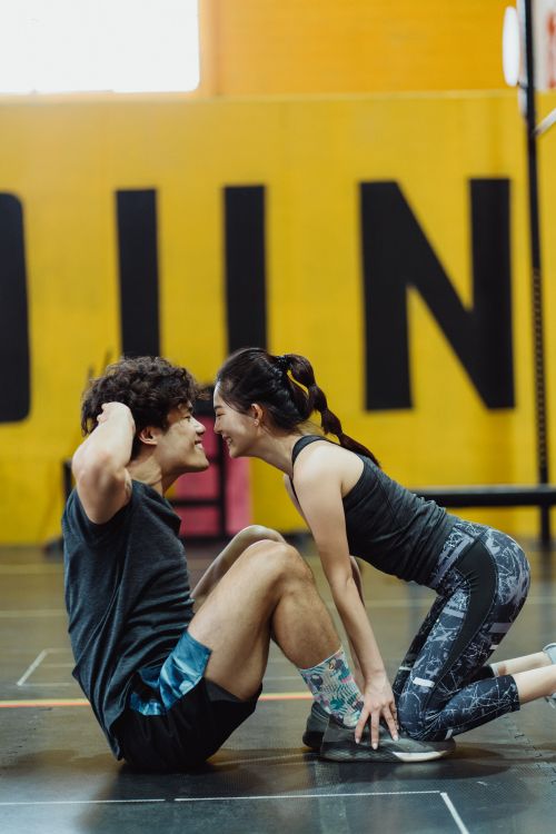 Free An Asian couple enjoys a fitness routine, enhancing closeness with sit-ups in a gym setting. Stock Photo