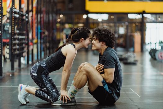 Side view of a happy couple bonding during a workout session in a gym setting.