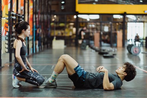 Free Asian couple engaged in workout session performing sit-ups in a well-equipped gym setting. Stock Photo