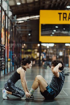Asian couple working out together in a gym, performing sit-ups and smiling, promoting fitness and togetherness.
