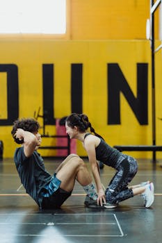 Fit Asian couple working out in a gym, focusing on sit-up exercises, promoting teamwork and fitness.