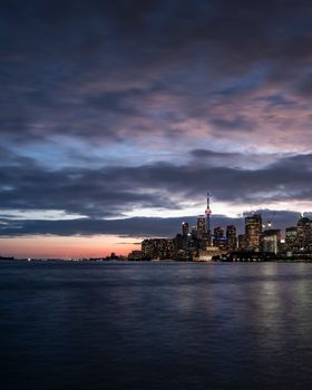 Modern illuminated city located on shore of sea against cloudy sundown sky in evening
