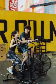 Happy couple enjoying a workout on stationary bikes in a vibrant gym setting.