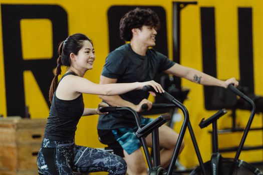 健身房里，亚洲男女面带微笑、精力充沛地骑着固定自行车锻炼