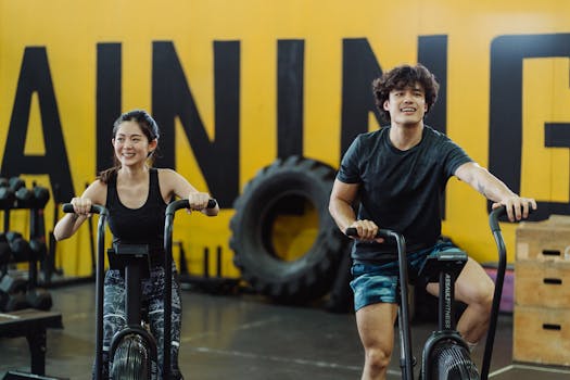 A man and woman enjoying a workout on indoor cycles at a gym, expressing fitness and joy.