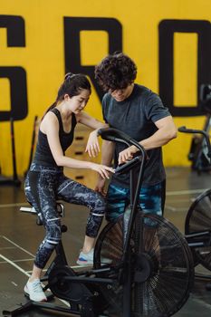 Asian couple engaging in fitness workout using elliptical trainer in gym.