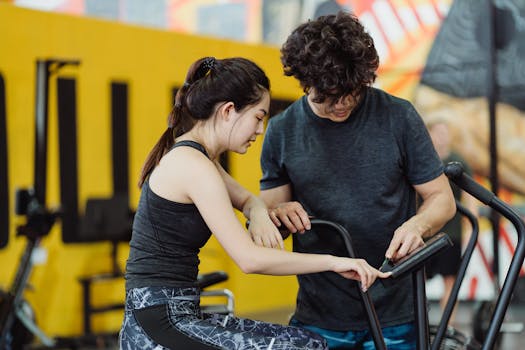 A couple in activewear setting up an elliptical trainer during a workout session in a modern gym.