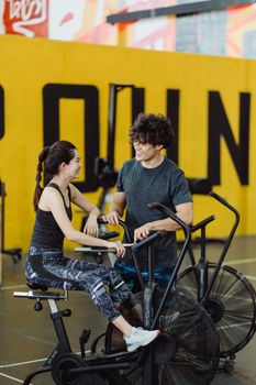 East Asian couple smiling during a workout on exercise bikes inside a gym.