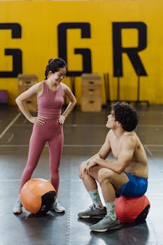 Fit couple taking a break at the gym, using medicine balls for support.